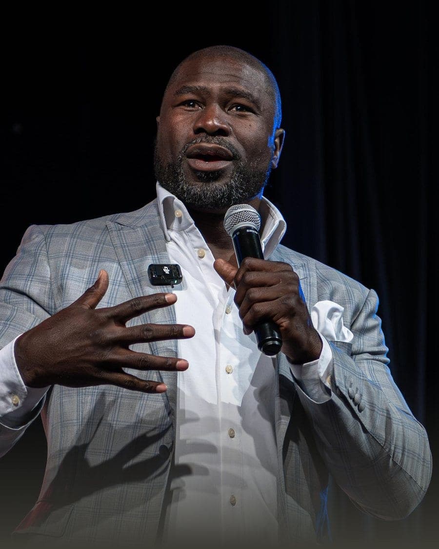 Ovie Mughelli speaking on stage with a handheld microphone
